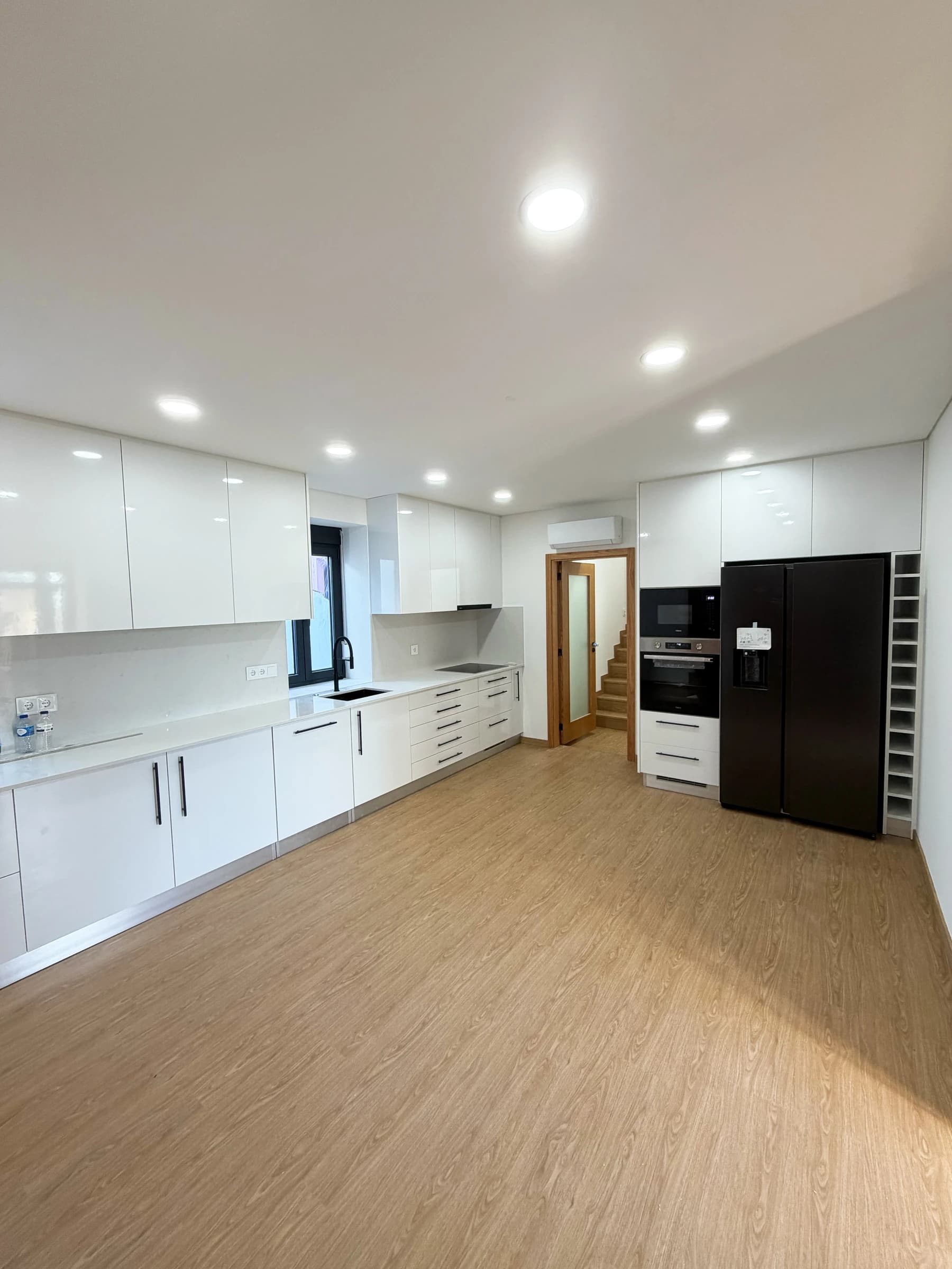 Cozinha moderna em open space em Estarreja, Aveiro, com mobiliário lacado branco, bancadas em quartzo e pavimento vinílico efeito madeira — remodelação VPObras