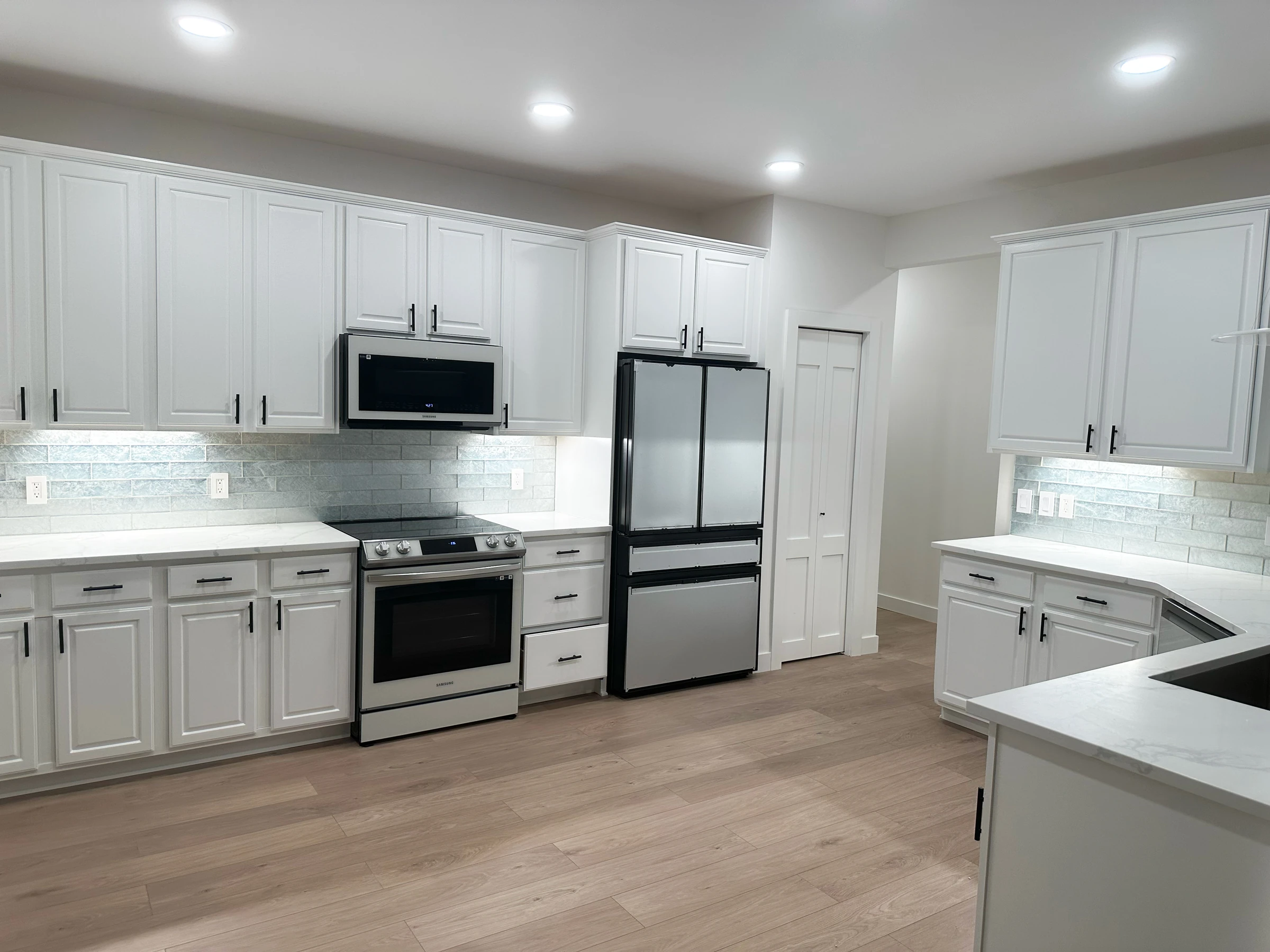 Vista da zona de confeção com bancada em quartzo, placa e forno encastrados e pavimento vinílico efeito madeira, cozinha Maple Grove Minnesota